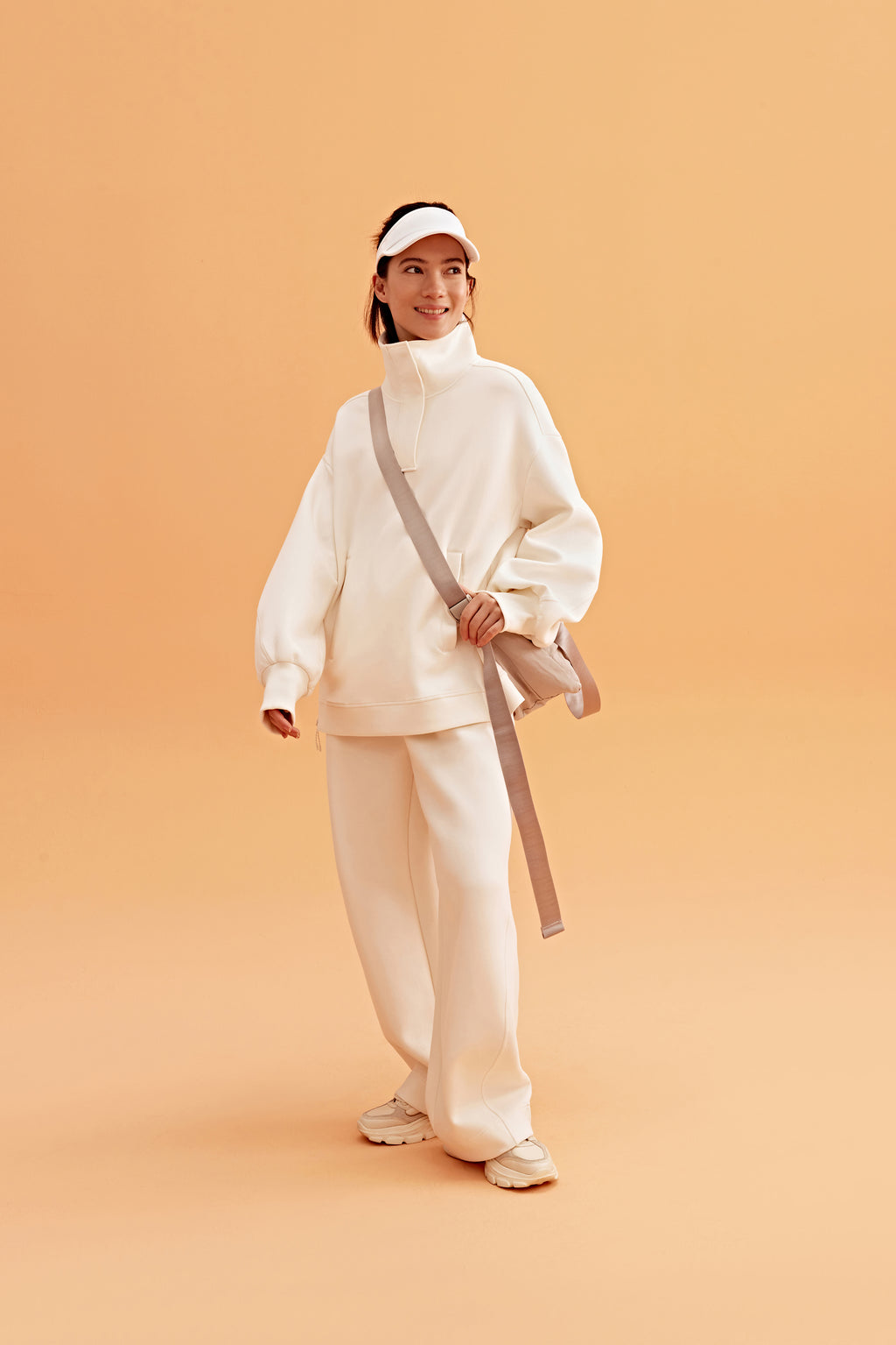 woman wearing a white visor and white half zip sweatshirt and white pants. pair with a white sneakers