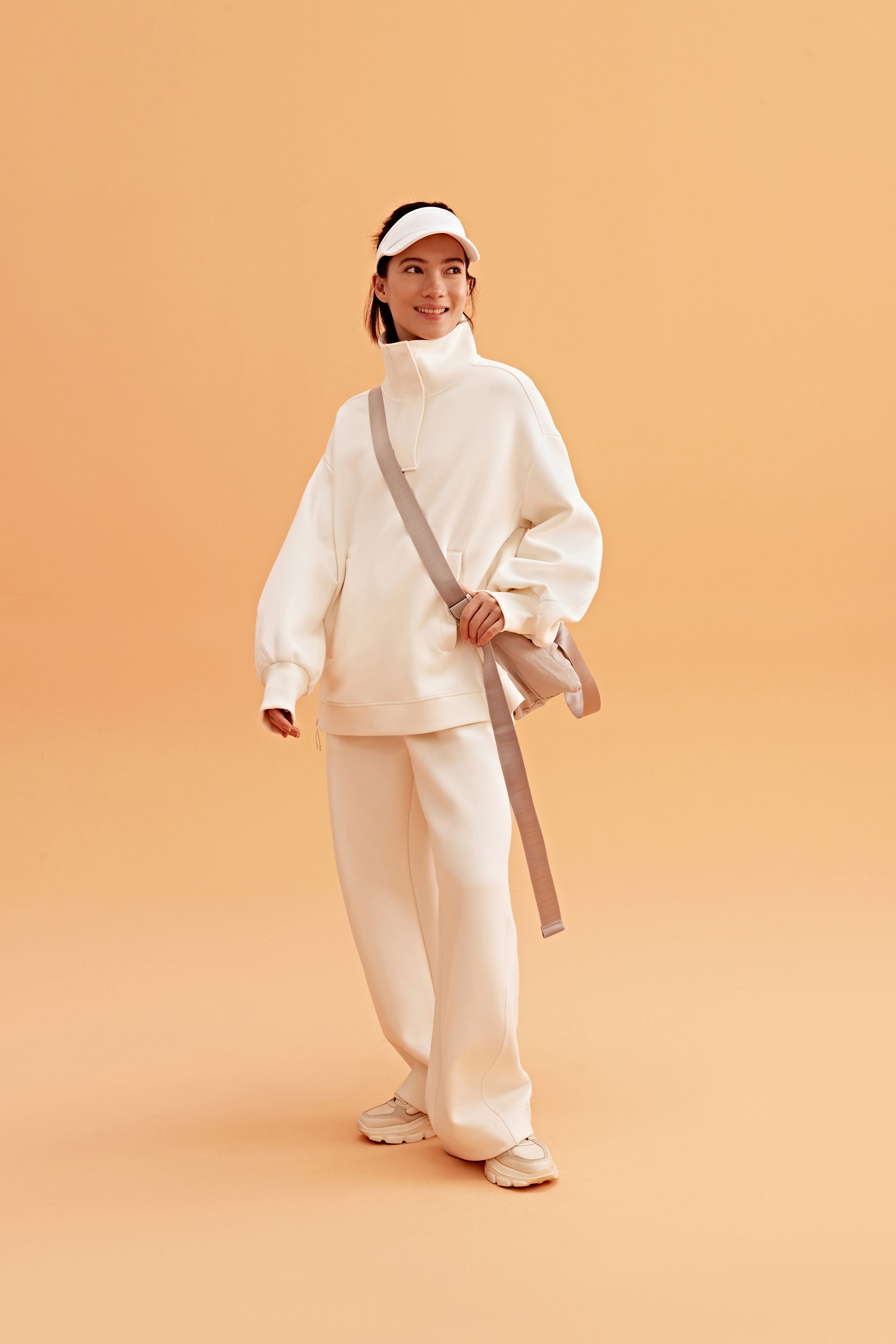 woman wearing a white visor and white half zip sweatshirt and white pants. pair with a white sneakers