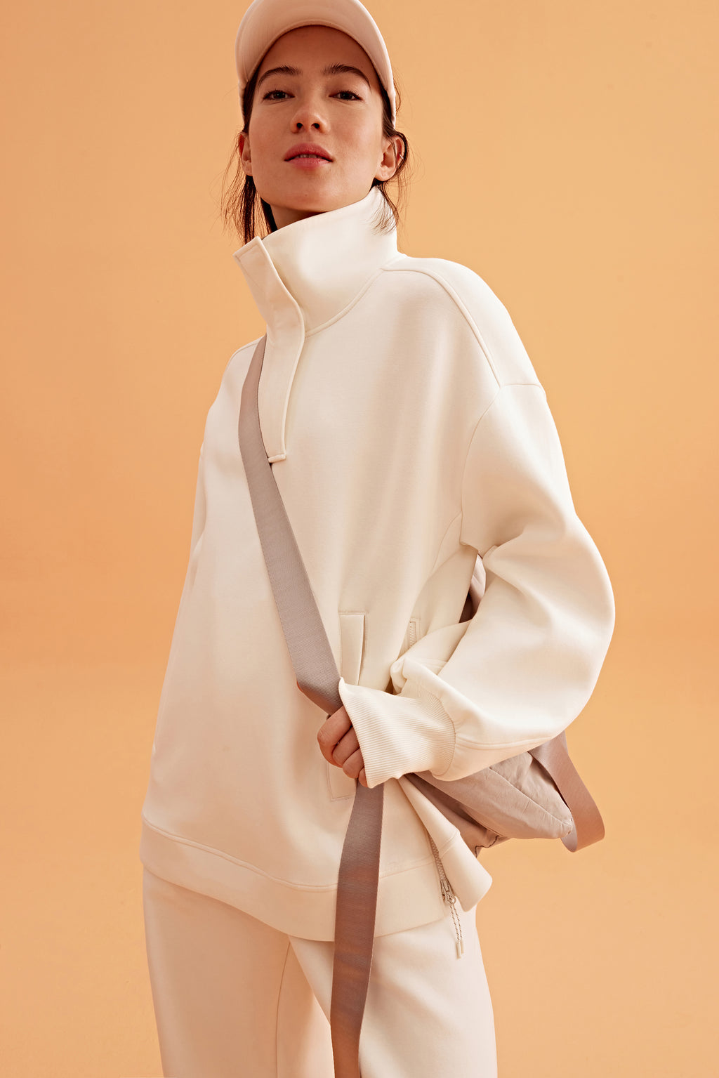 woman wearing a white visor and white half zip sweatshirt and white pants. pair with a light brown bag