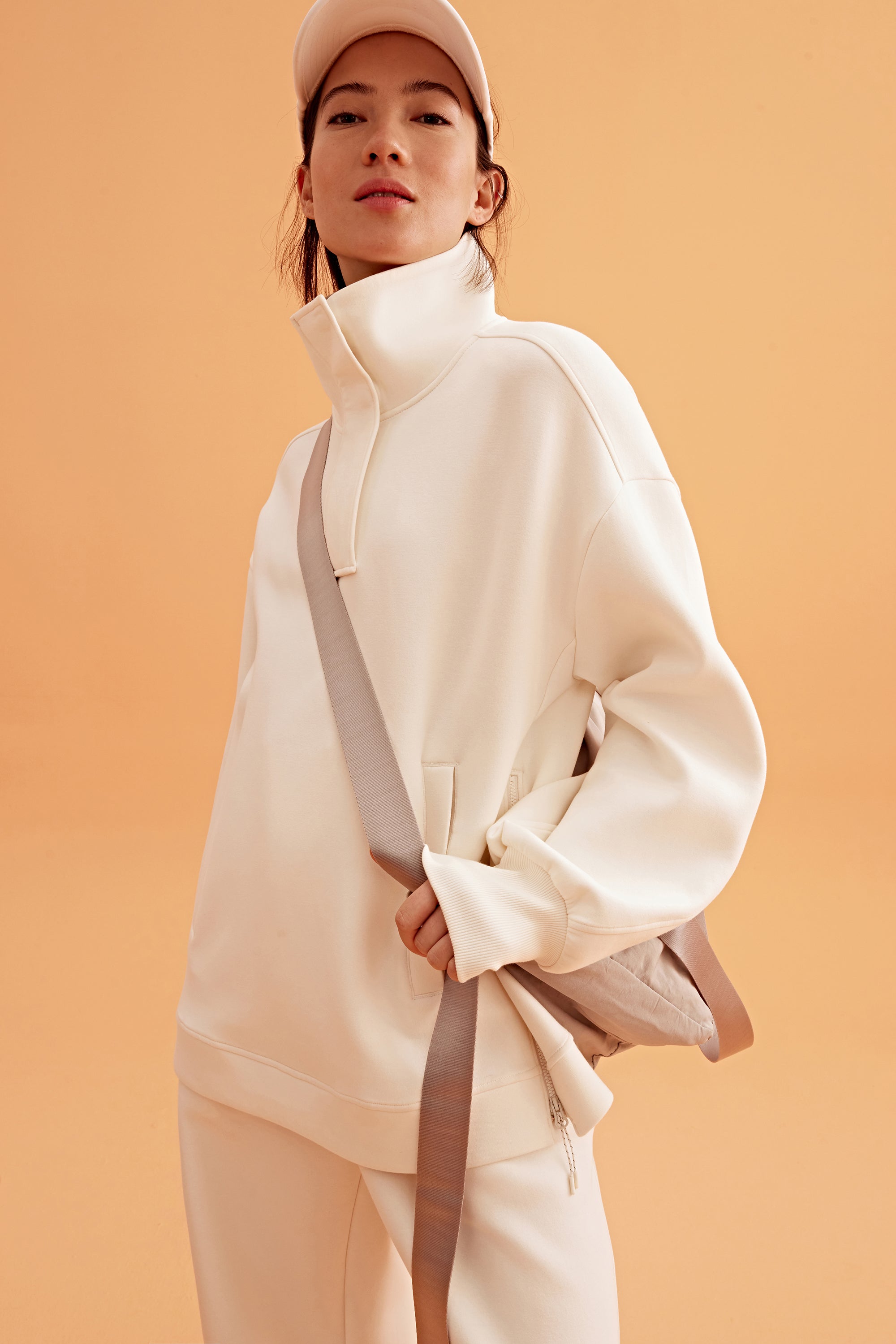 woman wearing a white visor and white half zip sweatshirt and white pants. pair with a light brown bag