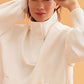 woman wearing a white visor and white half zip sweatshirt and white pants.