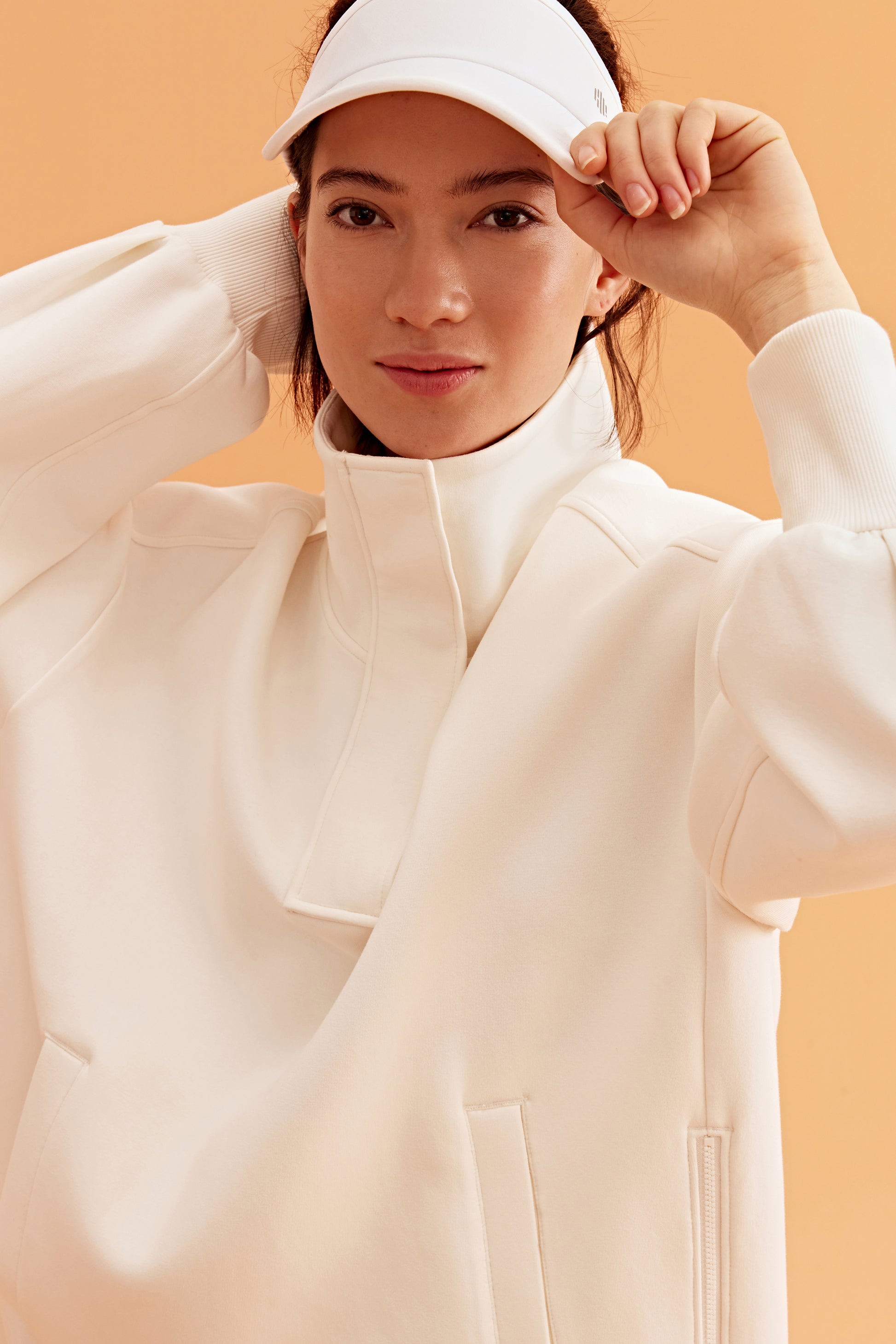 woman wearing a white visor and white half zip sweatshirt and white pants.