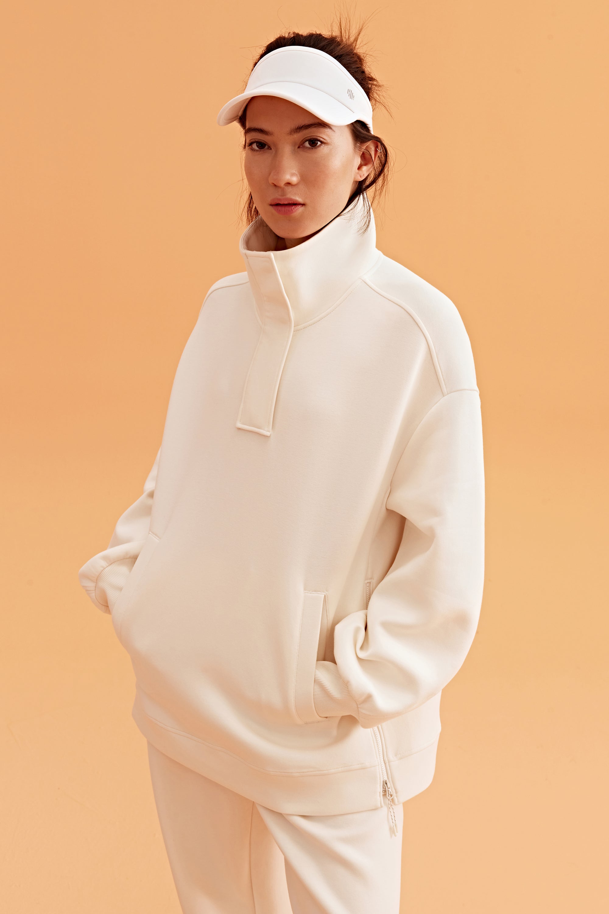 woman wearing a white visor and white half zip sweatshirt and white pants.
