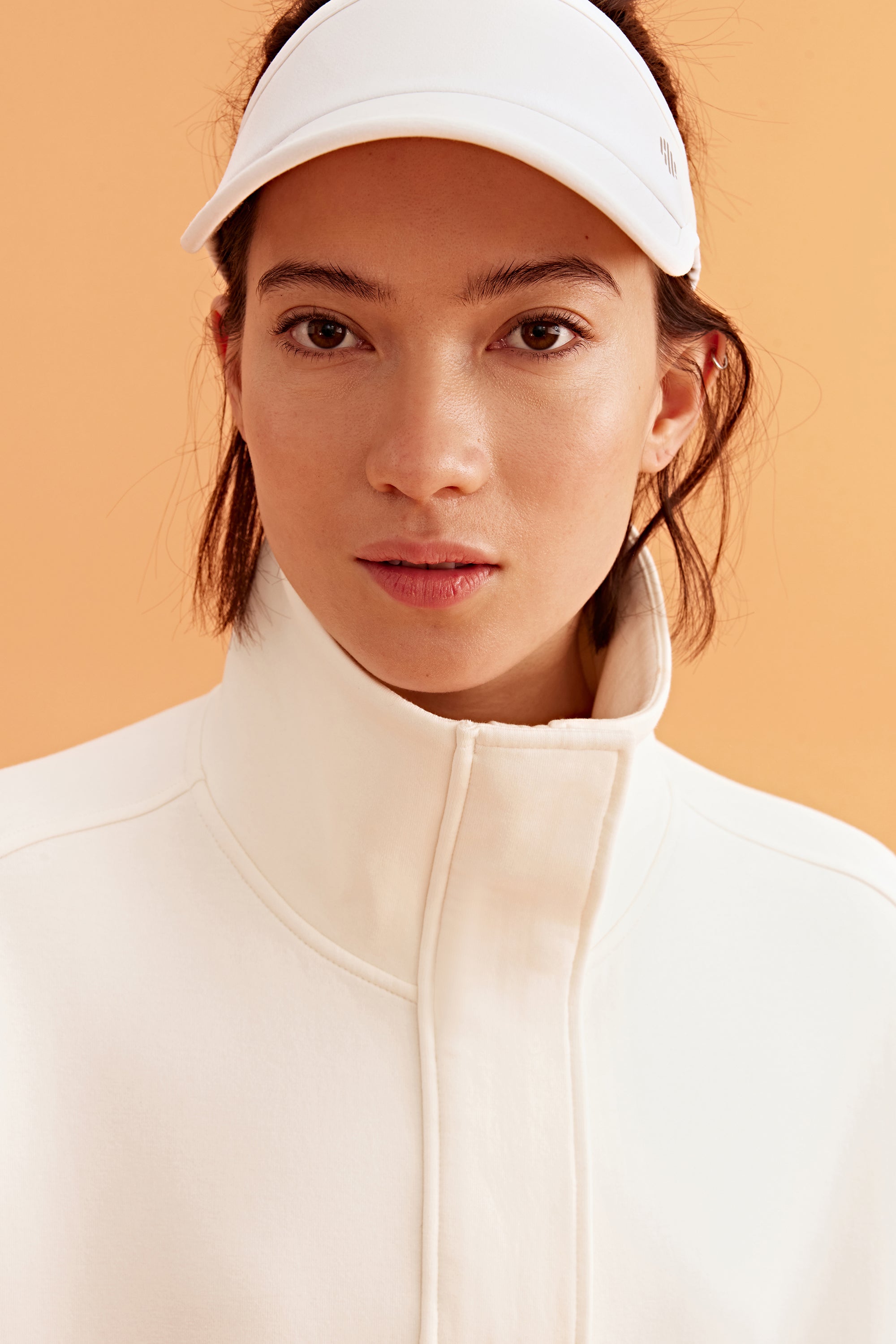 closeup shot of woman wearing a white visor and white sweatshirt 