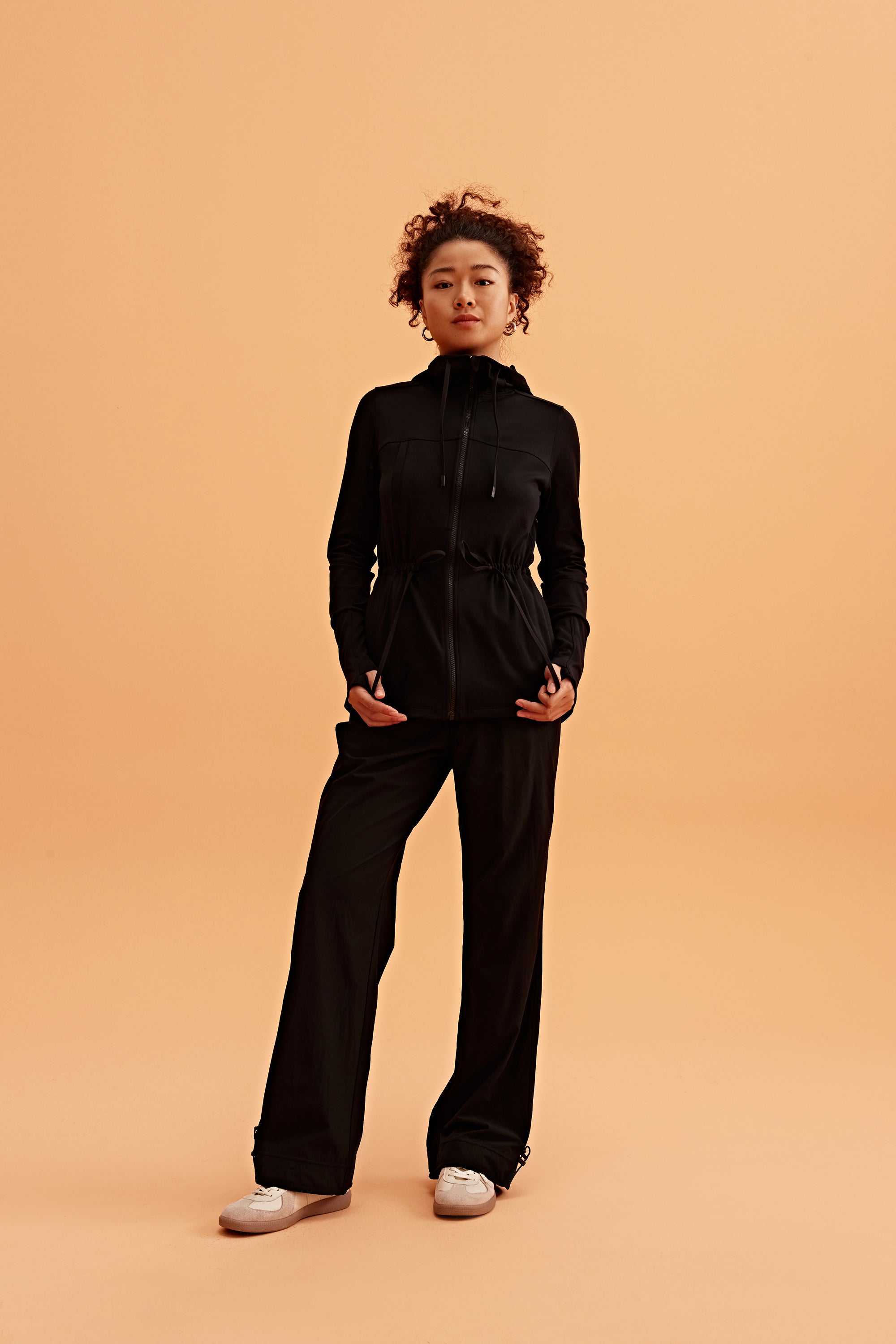 a woman wearing a light black hooded jacket and black pants