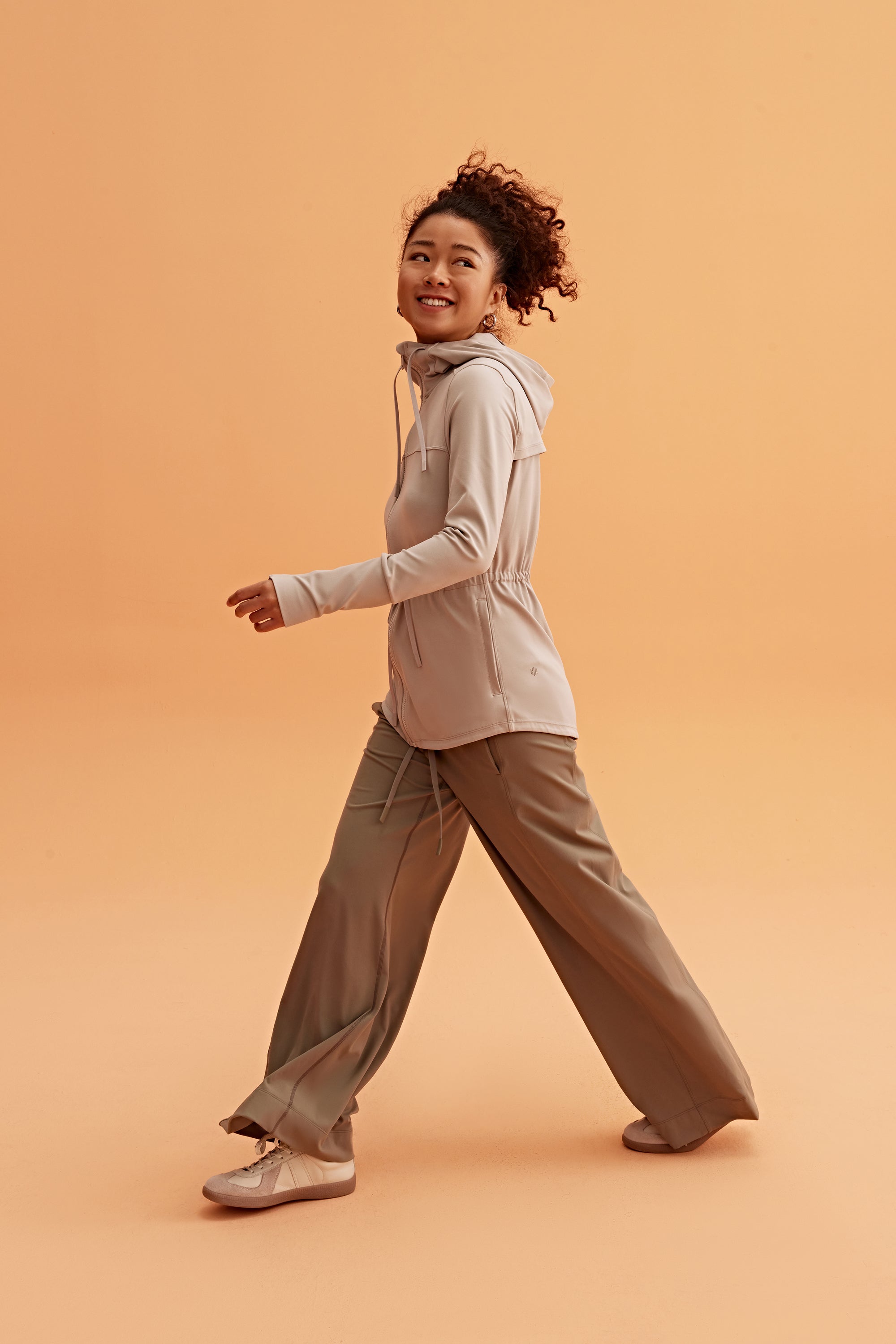 a woman wearing a light brown hooded jacket and brown pants