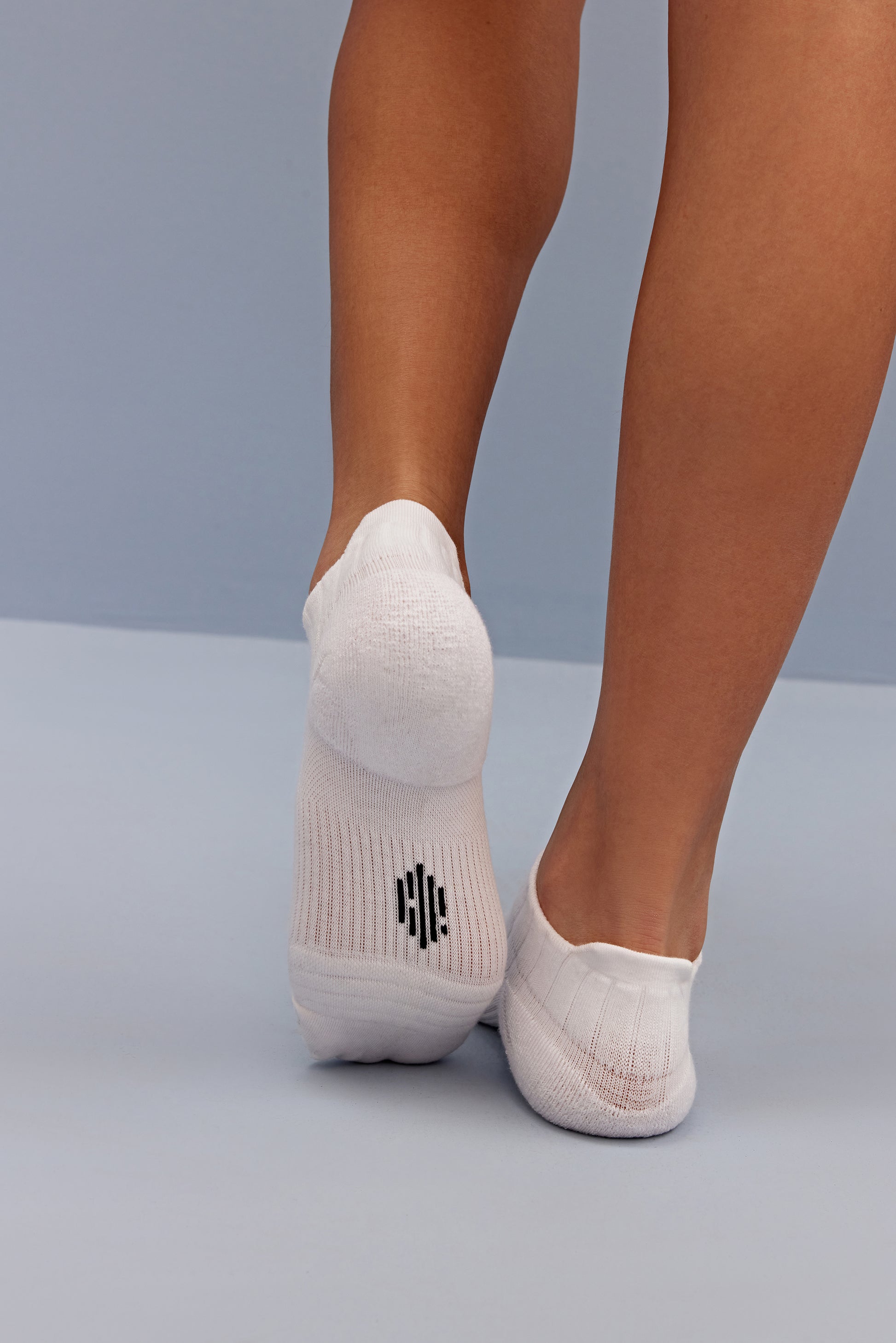 a person wearing white socks, lifting left foot to show the neiwai active logo