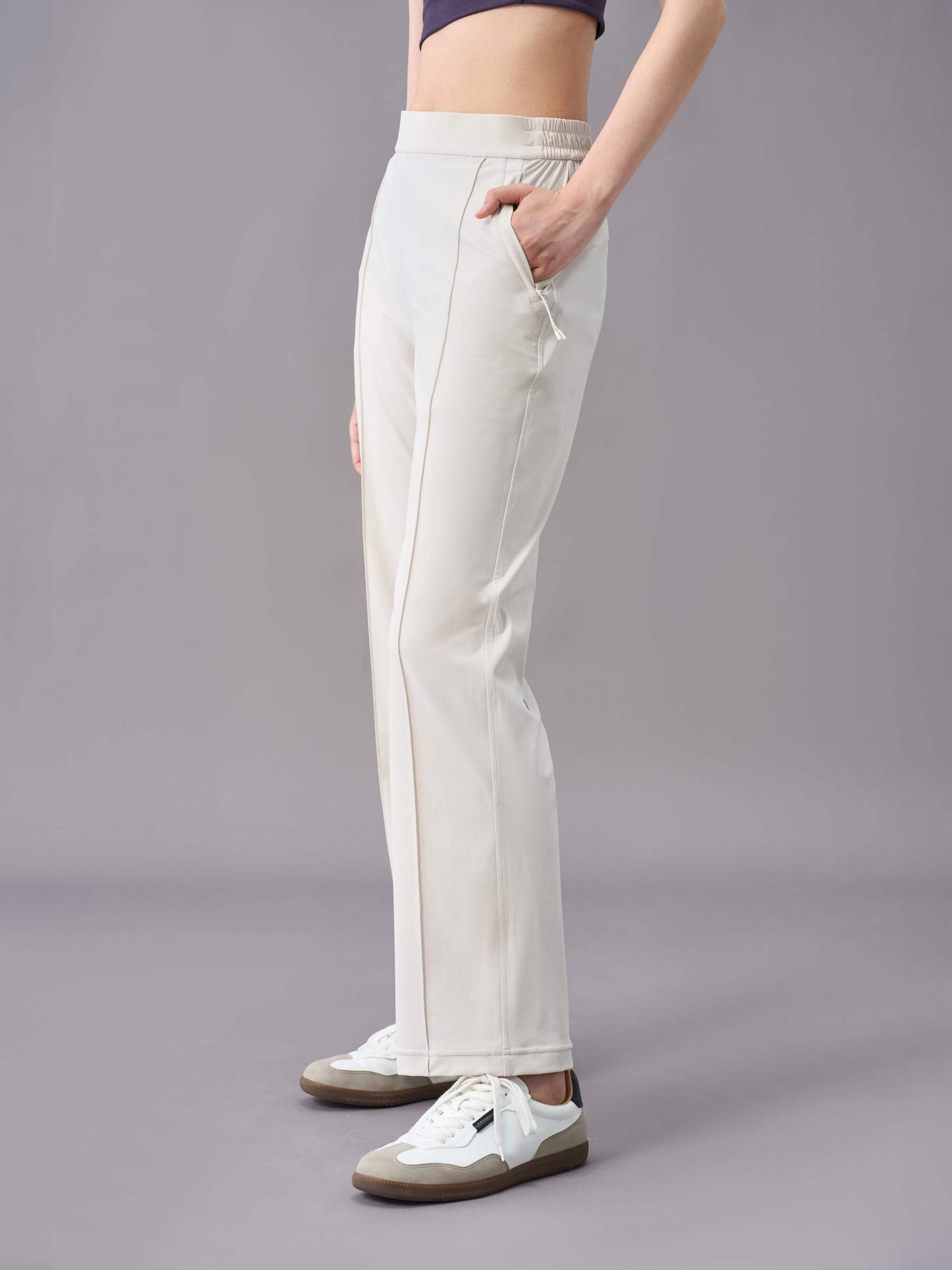 A side view of a model wearing off-white straight-leg pants, paired with white sneakers. The pants feature a relaxed fit with a drawstring waistband, side pockets, and subtle seam details down the front.