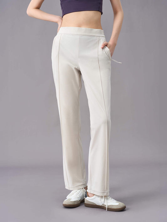 A model wearing off-white straight-leg pants, paired with white sneakers. The pants feature a relaxed fit with a drawstring waistband, side pockets, and subtle seam details down the front.