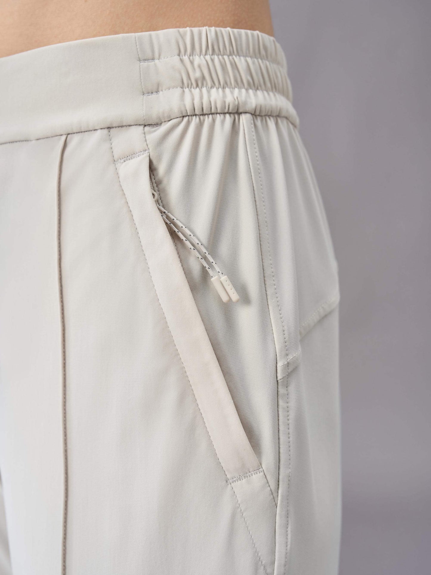 A close-up view of off-white pants, highlighting the elastic waistband and side pocket with drawstring detail. The fabric and stitching details are clearly visible, showcasing the design