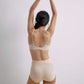 Back view of a model wearing a nude 3/4 cup bra and high-waisted seamless briefs, with the model’s arms raised, showcasing the bra’s adjustable straps, back closure, and the smooth fit of the briefs.