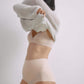 Side view of a model wearing a nude 3/4 cup bra and high-waisted seamless briefs, pulling a cozy white sweater over her head, highlighting the smooth fit and comfortable layering.