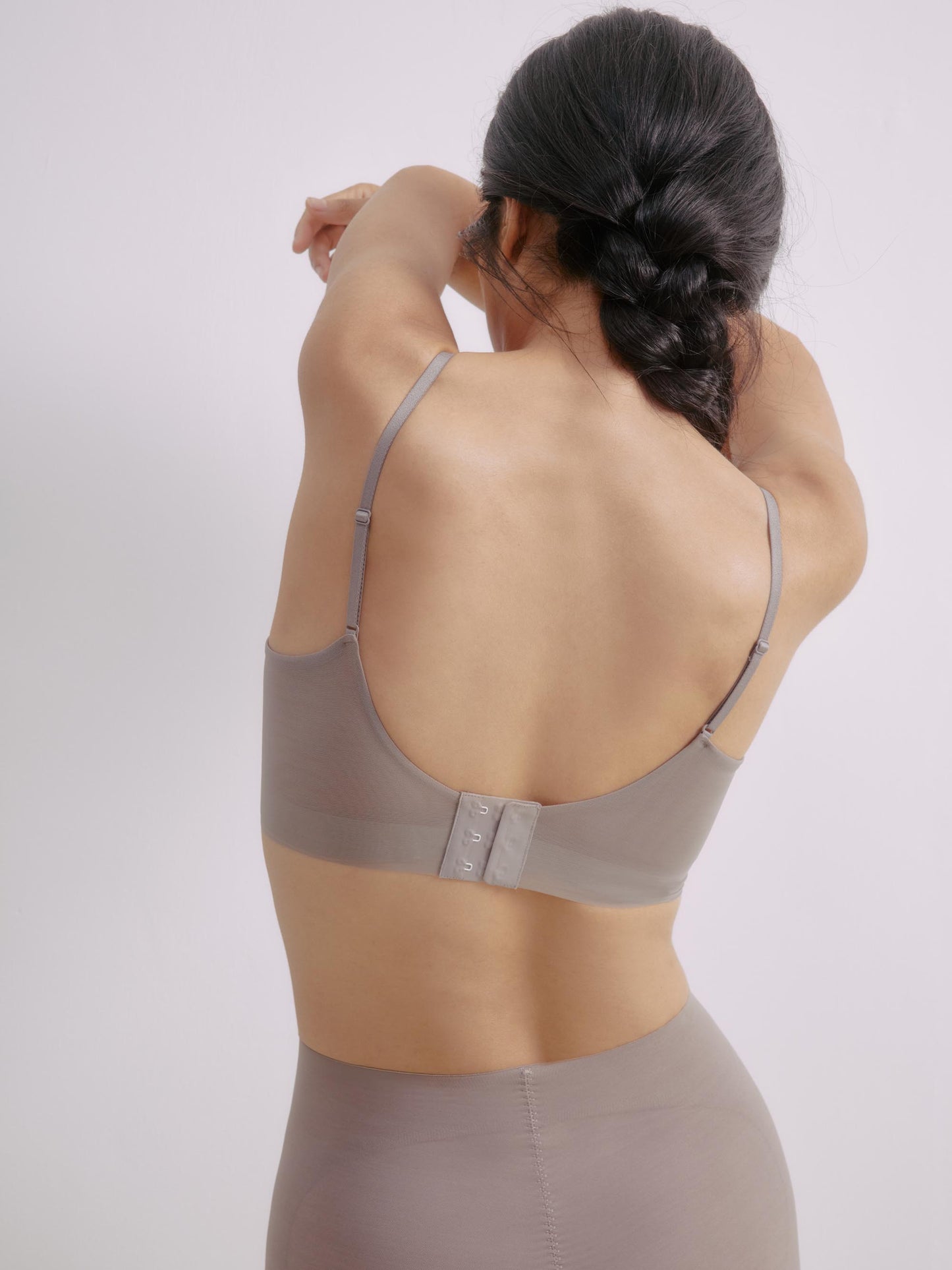 Back view of a model wearing a gray purple bra with adjustable straps and a back closure, arms extended forward, highlighting the bra’s supportive fit and mesh detailing.