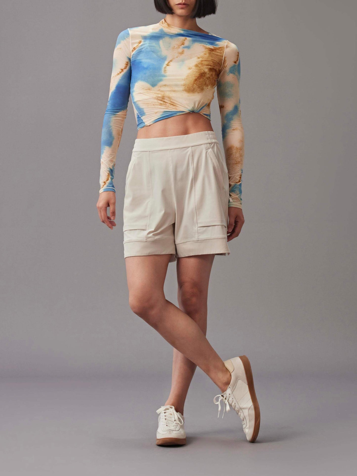 Person wearing an asymmetric crop top paired with beige shorts and white sneakers.