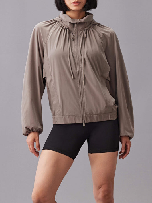 A model wearing a taupe zip-up sunblock jacket, paired with black high-waisted shorts.