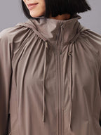 Front view of a model wearing a taupe hooded jacket with a full front zipper and drawstring details.