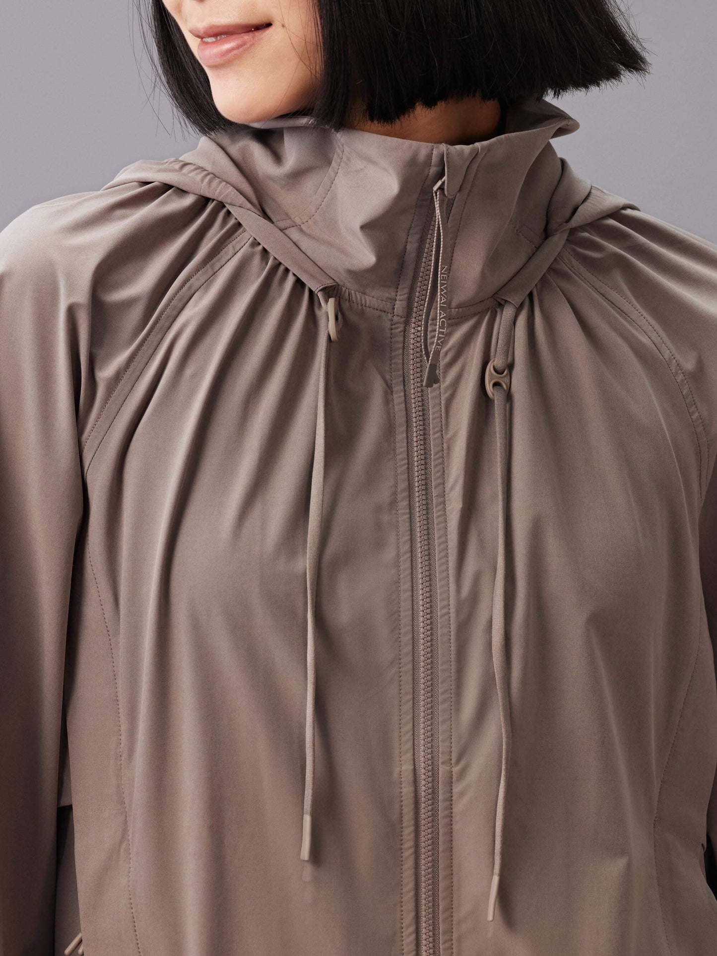 Front view of a model wearing a taupe hooded jacket with a full front zipper and drawstring details.