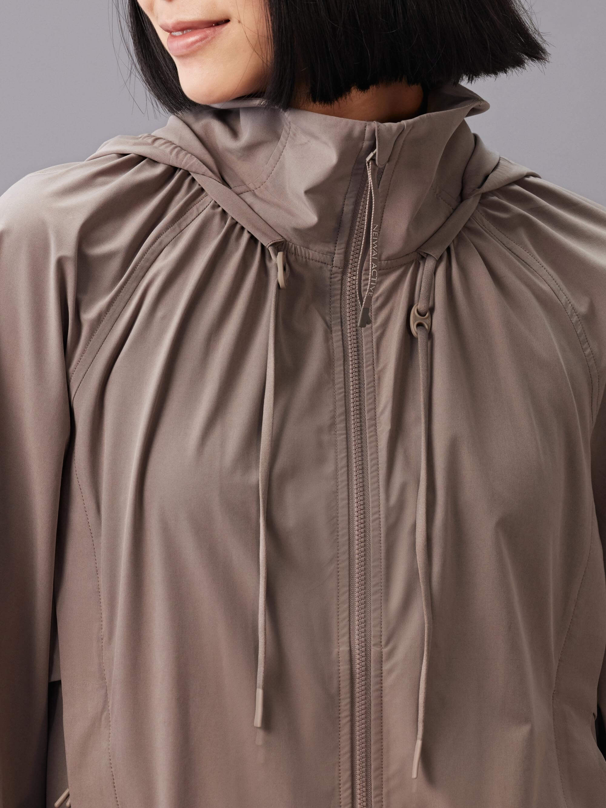 Front view of a model wearing a taupe hooded jacket with a full front zipper and drawstring details.