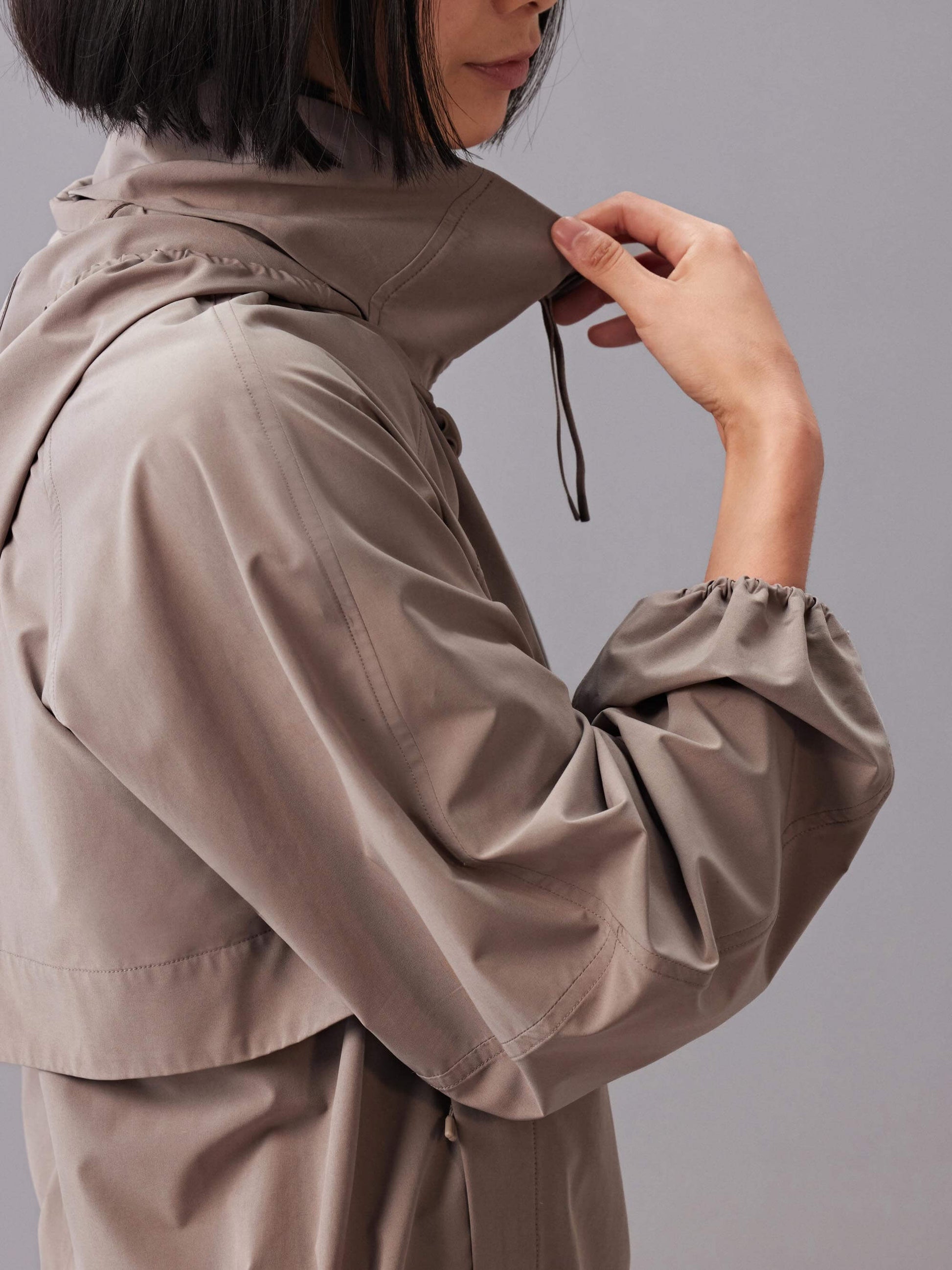 A side view of a model wearing a taupe zip-up sunblock jacket.