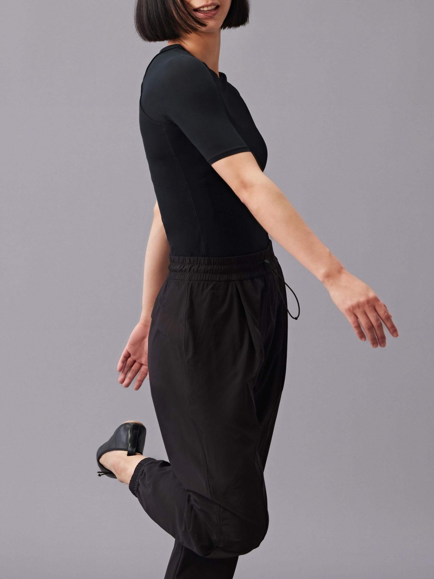 The side of a woman wearing black short sleeve T-shirt and black pants, lifting one leg up. 