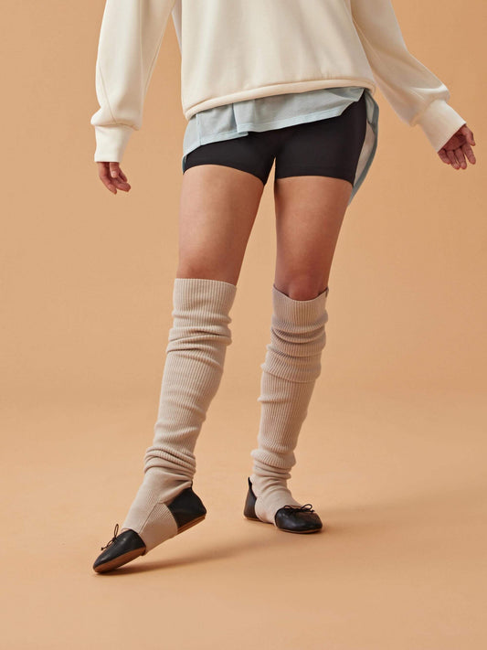 View of bottom half of woman wearing a white sweatshirt over a blue shirt, black shorts, and beige leg warmers