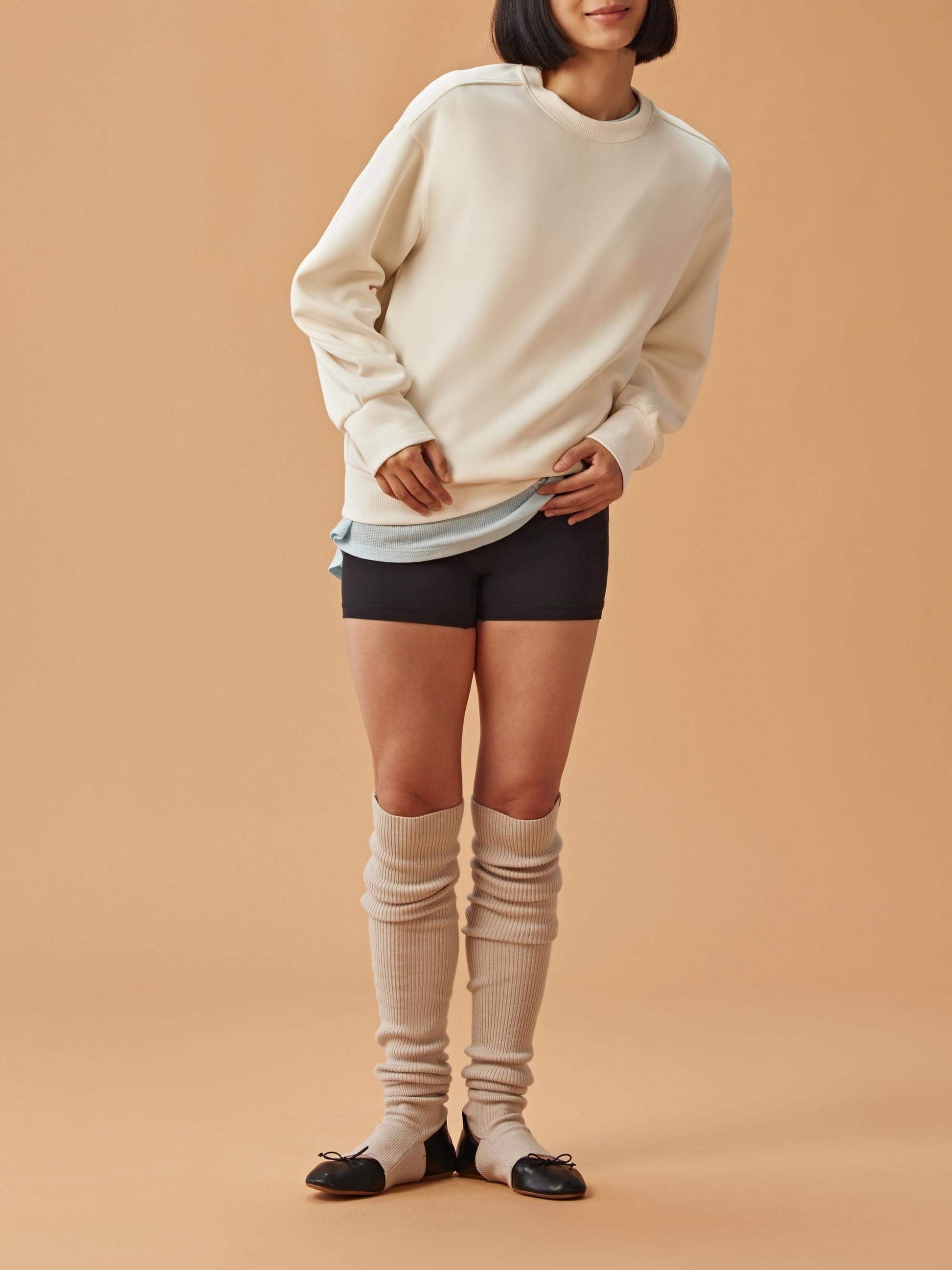 Woman wearing a white sweatshirt over a blue shirt, black biker shorts, and beige leg warmers