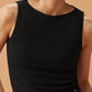 A women wearing a black sleeveless top with a ribbed lower section, standing against a warm beige background.