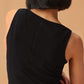 Back view of woman wearing a black sleeveless top with a ribbed lower section, viewed from the back, against a warm beige background.