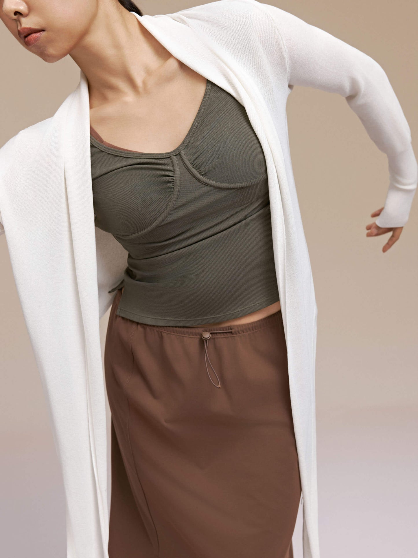 Front view of woman wearing olive green long sleeve top with white cardigan.