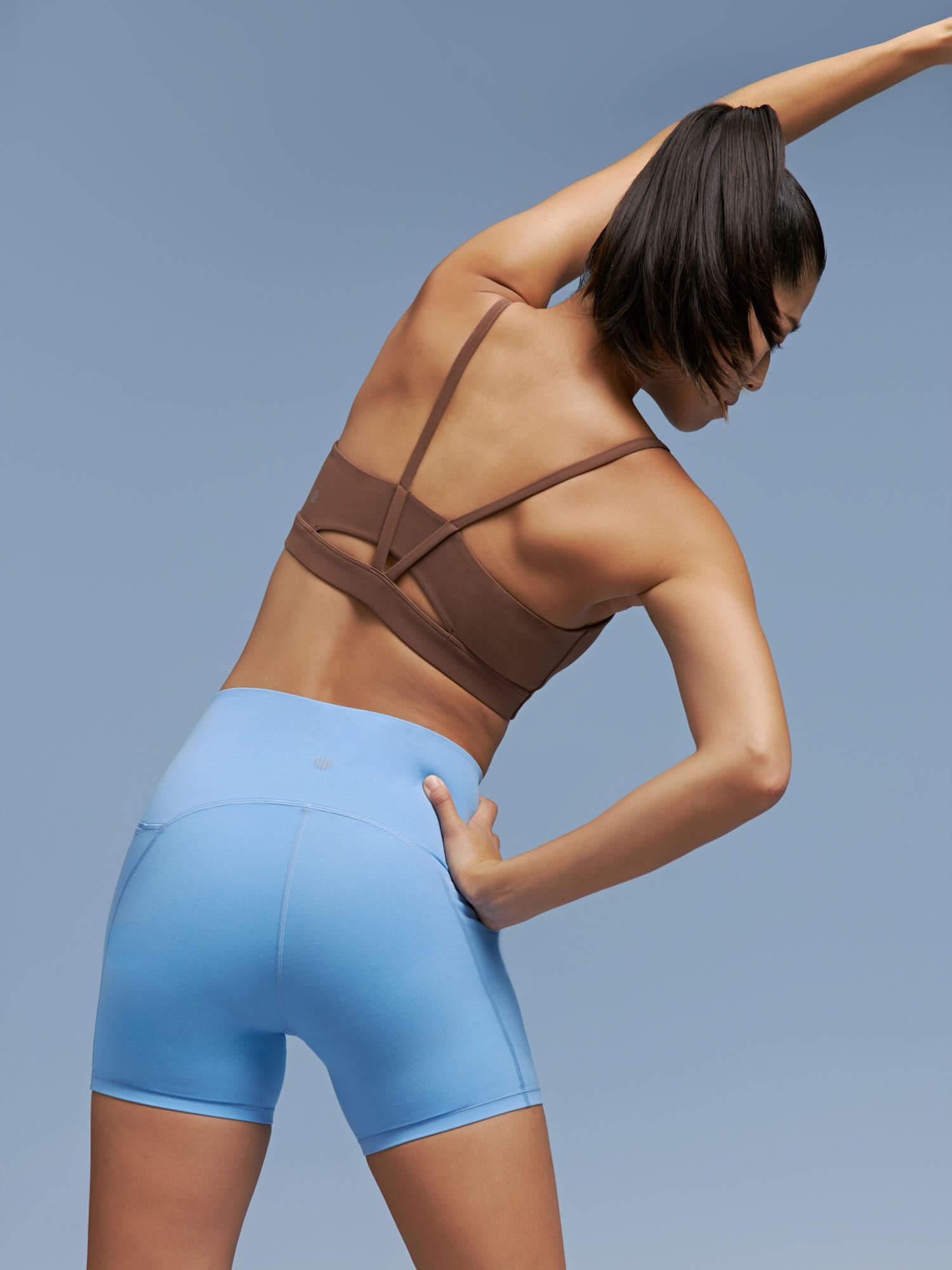 Back side of woman wearing brown sports bra and light blue biker shorts