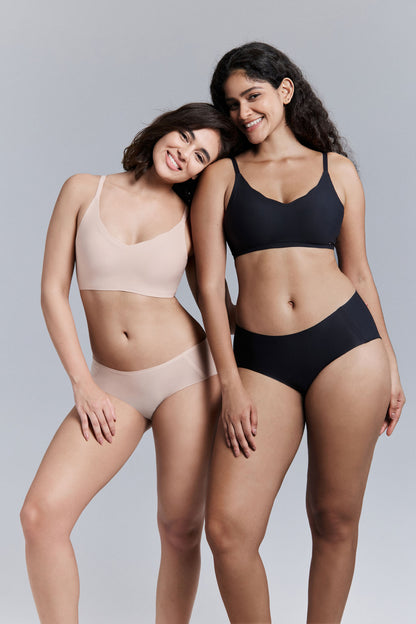 Two women wearing beige and black bra and brief set against a gray background.