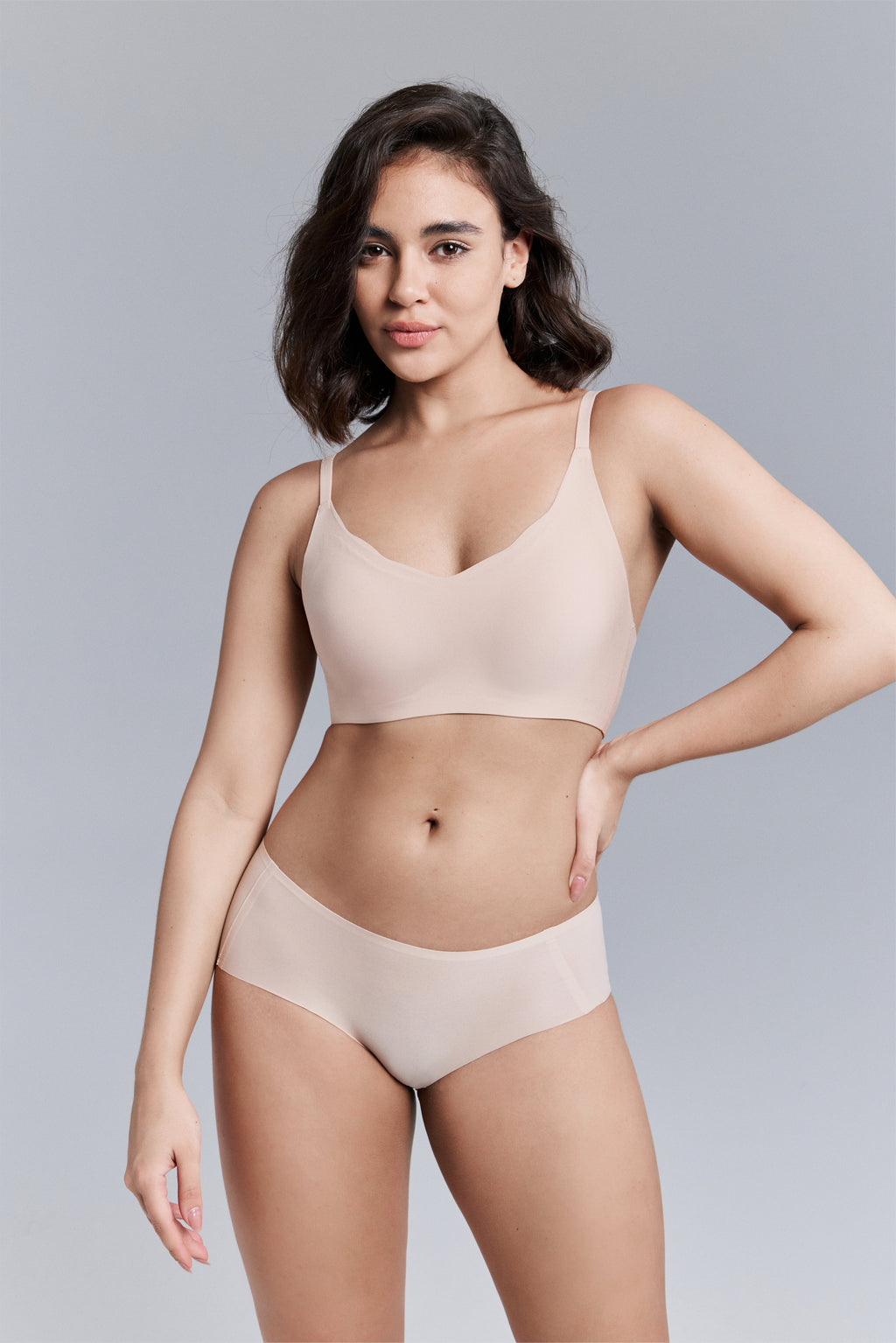 Model wearing a beige bra and panties set against a gray background