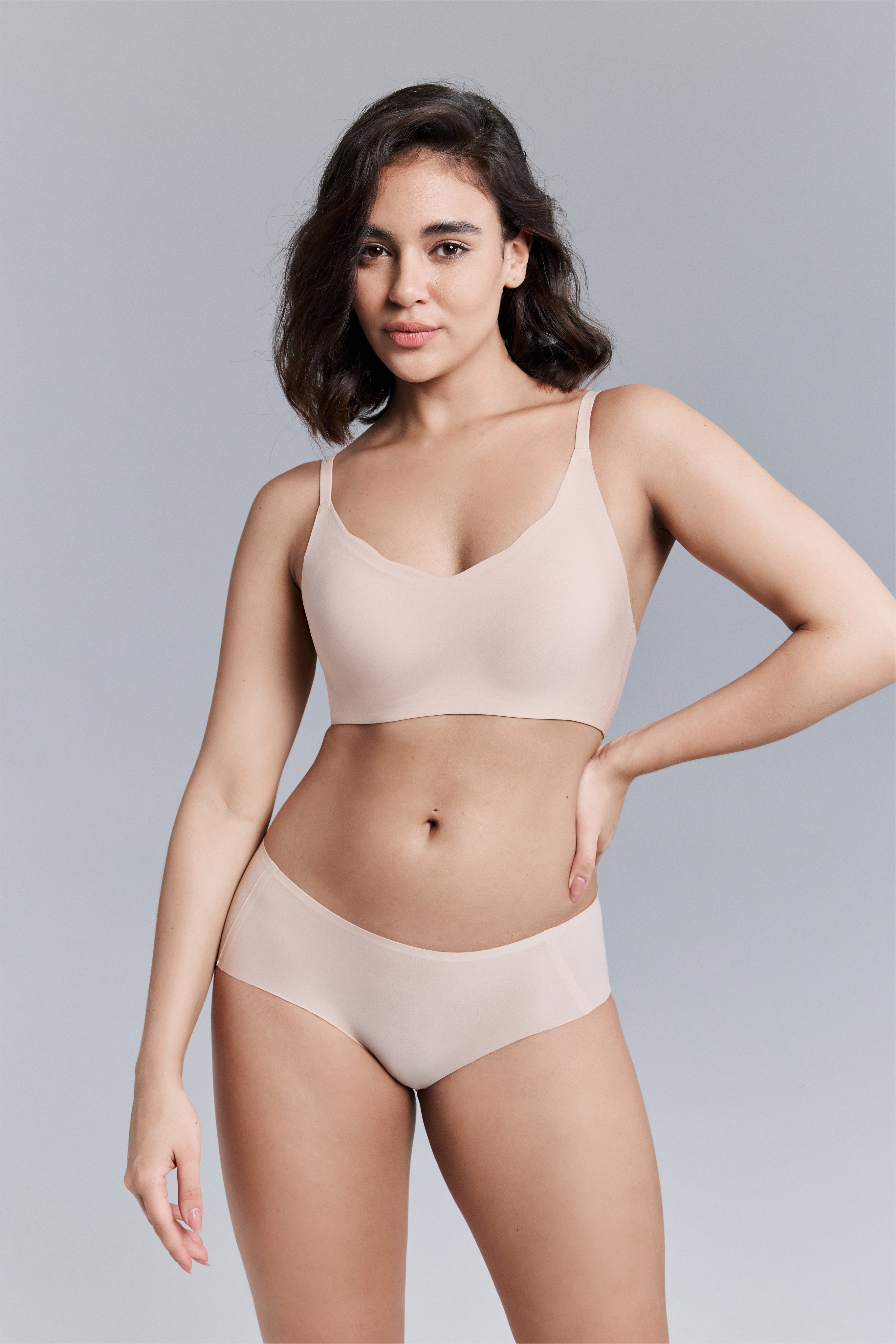 Model wearing a beige bra and panties set against a gray background