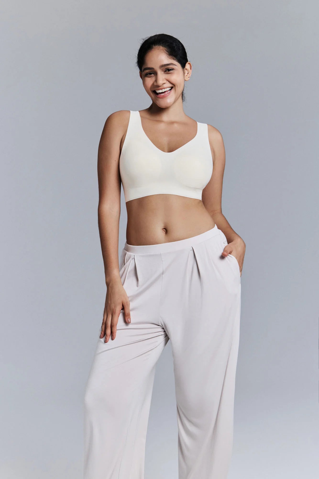 Woman wearing a white sports bra and pants on a gray background