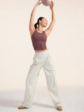 Woman in a brown tank top and white pants holding a pink ball