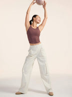 Woman in a brown tank top and white pants holding a pink ball