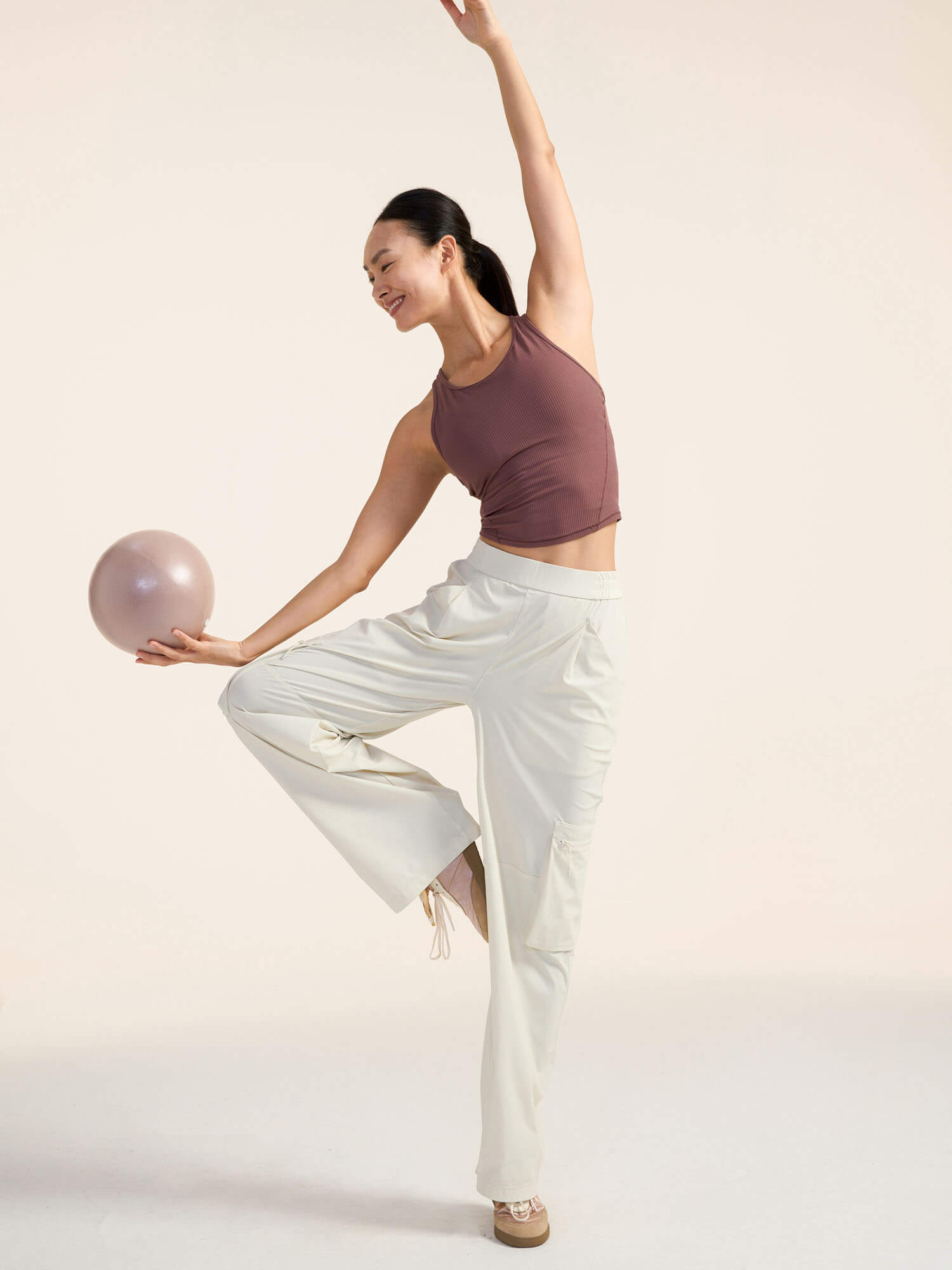 Woman in a yoga pose holding a pink ball 