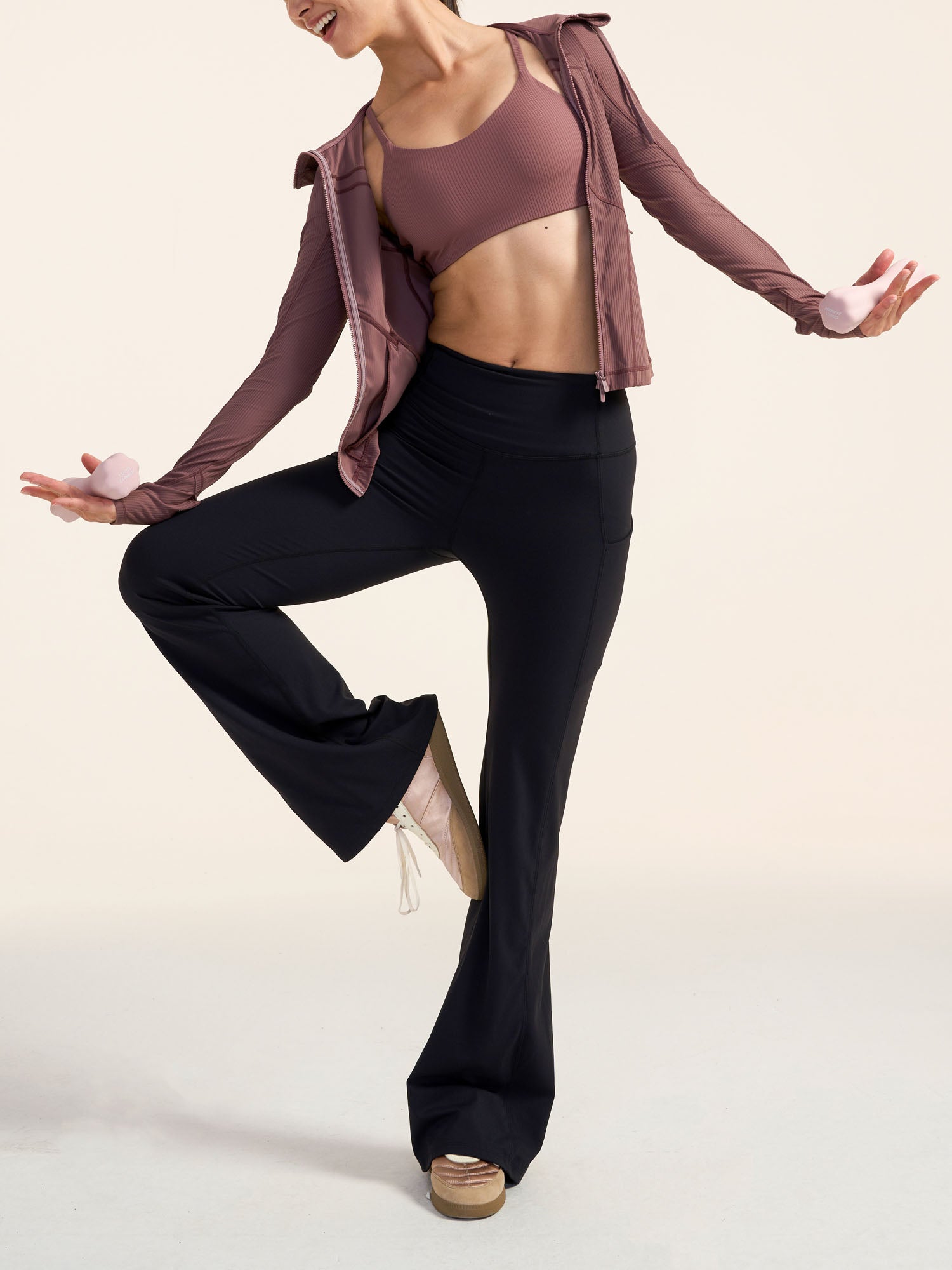Model wearing a mauve sports bra and jacket with black yoga pants on a beige background