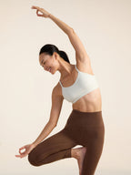 Model in white sports bra and brown leggings posing against a beige background
