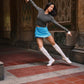 Dancer wearing blue skort, gray hoodie, and gray leg warmers