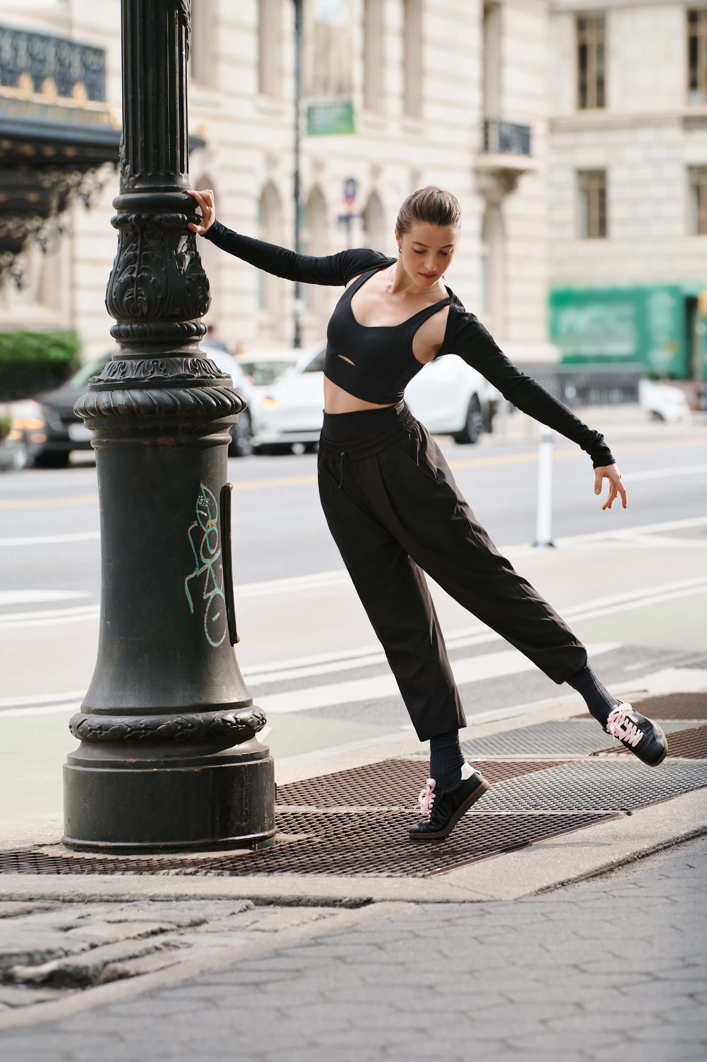 Dancer wearing long black sports bra, ballet shrug, and black joggers over black leggings