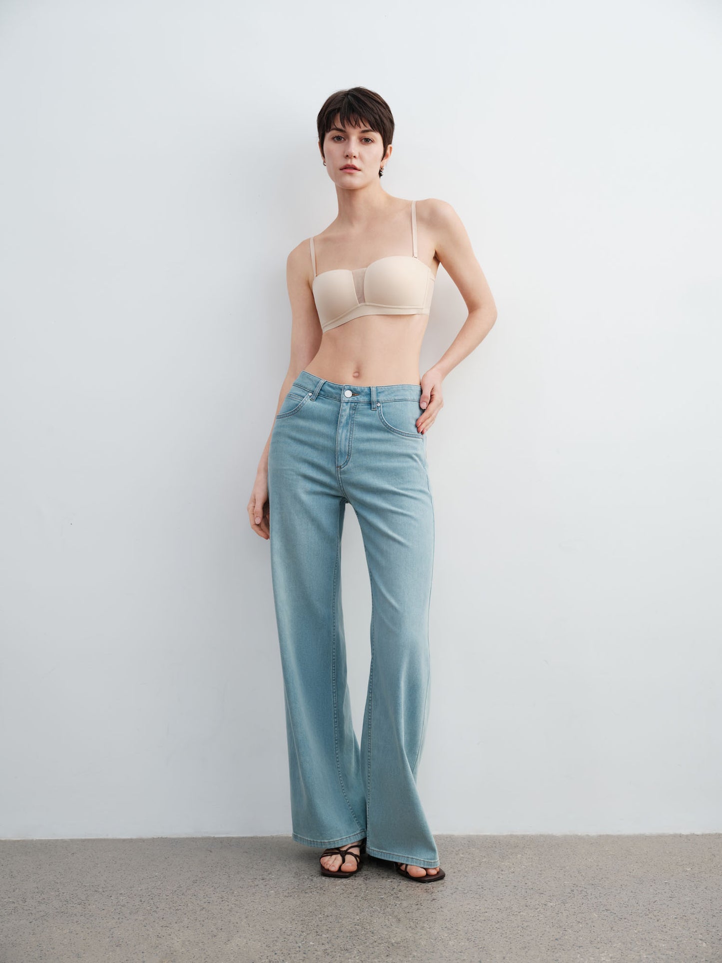 Model wearing a beige strapless top and light blue flared jeans against a plain background.
