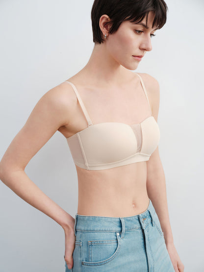 Model wearing a beige bra and light blue jeans against a plain background.