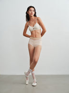 Model wearing a white bra and brief set with white socks and shoes on a plain background
