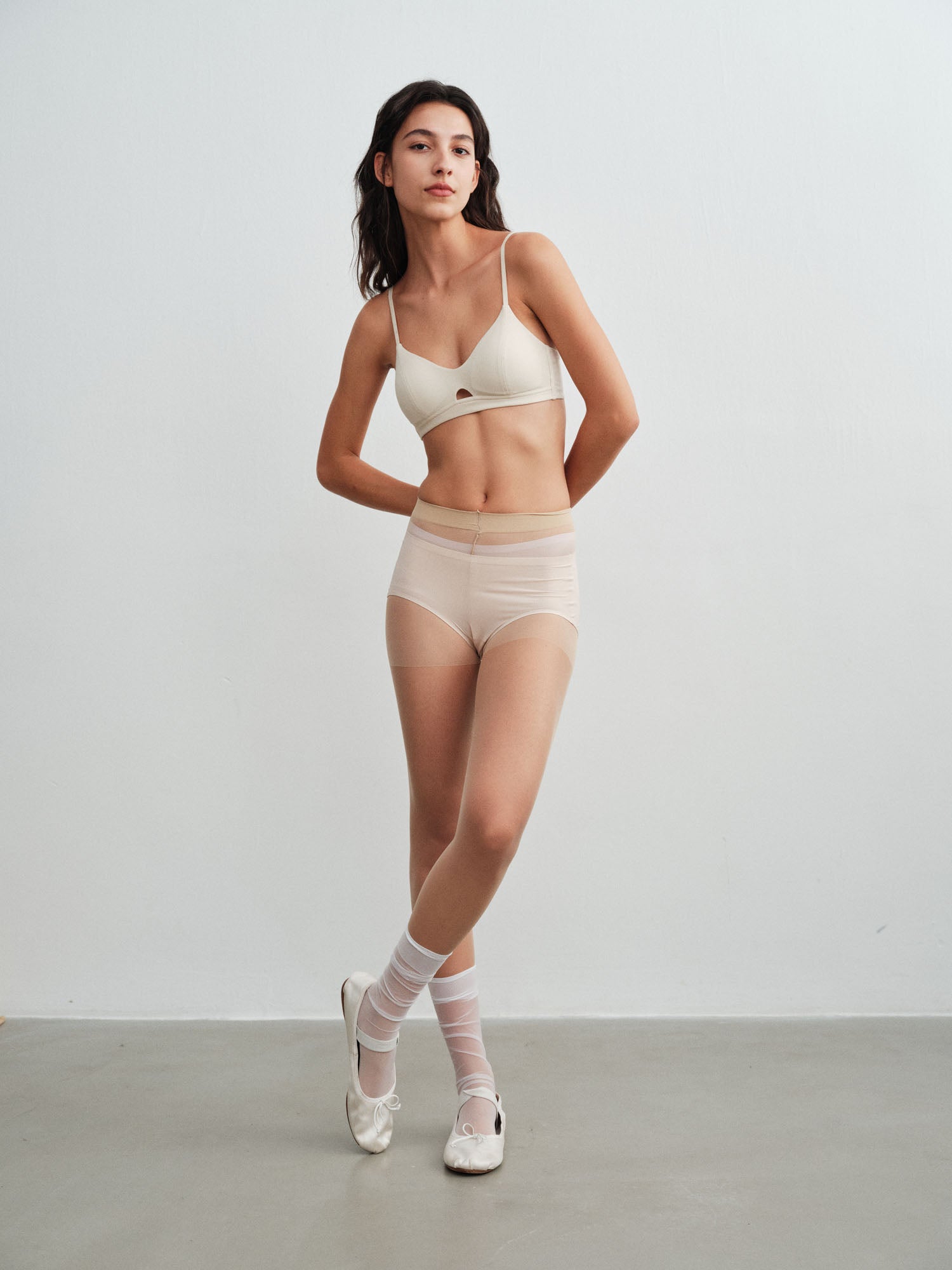 Model wearing a white bra and brief set with white socks and shoes on a plain background