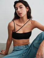 Model wearing a black strappy bra top and blue jeans against a plain background.