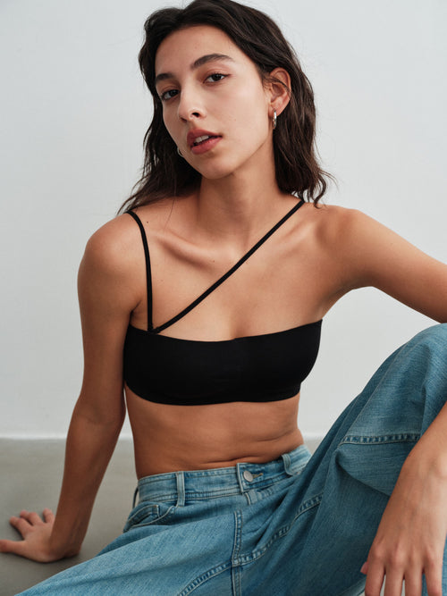 Model wearing a black strappy bra top and blue jeans against a plain background.