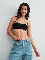 Model wearing a black bra and blue jeans against a light gray background. 