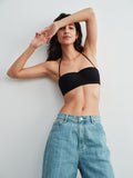 Model wearing a black bra top and blue jeans against a white  background.