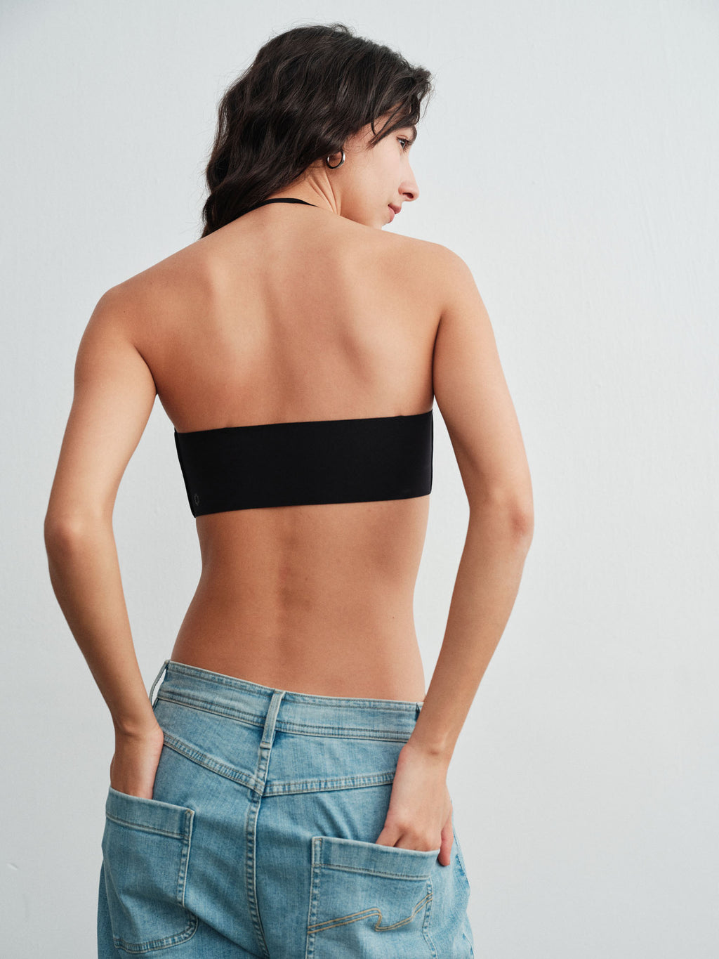 Model wearing a black strapless top and blue jeans on a light gray background. 